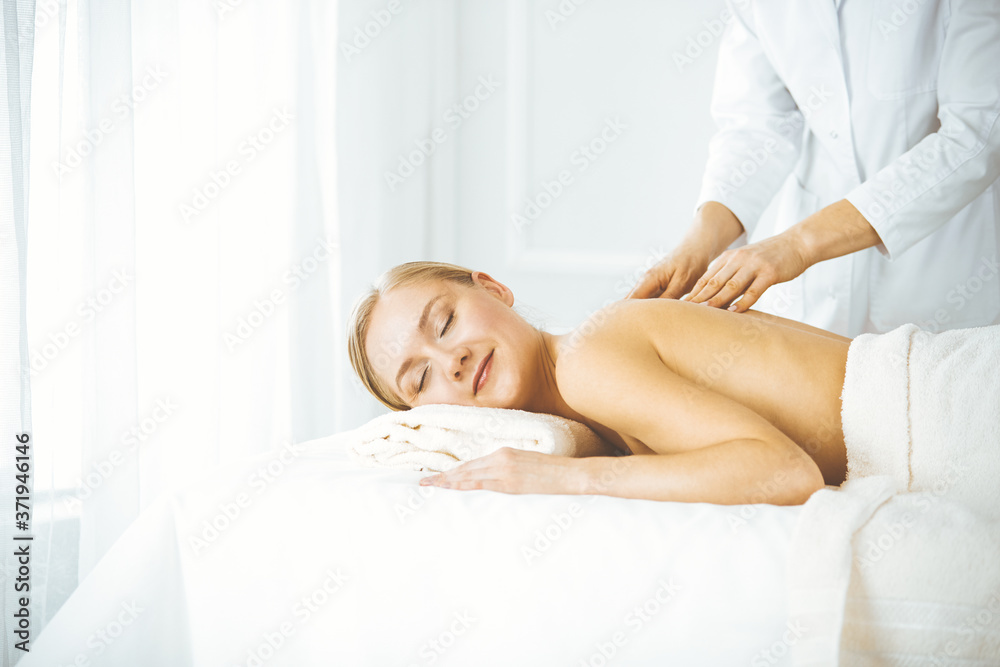Fototapeta premium Beautiful happy woman enjoying back massage with closed eyes. Beauty and Spa salon concept