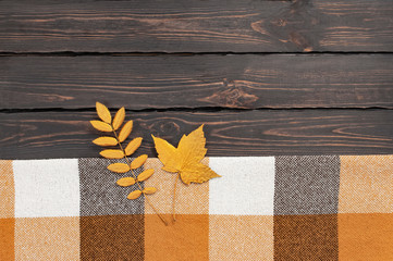 Woolen checkered plaid. Autumn background. Checkered yellow brown plaid with golden leaves on dark wooden background top view copy space Cozy fall composition Autumn textile, checkered fabric texture