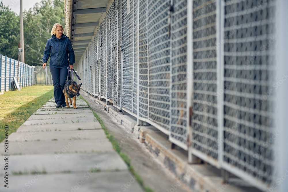 Female officer with security dog walking by locked cages