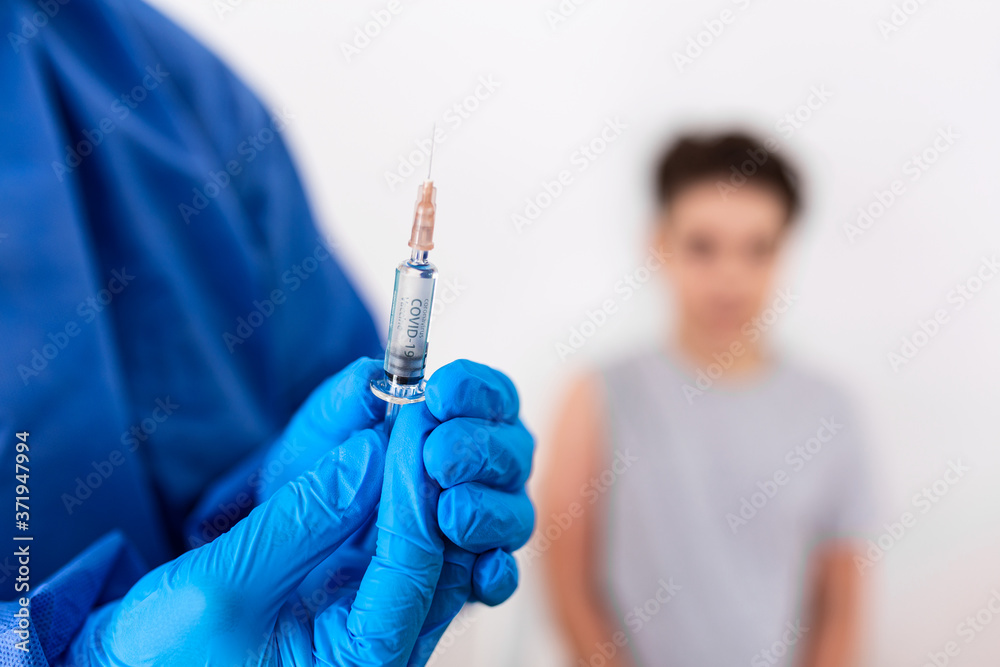 Vaccination. Professional doctor in blue sterile gloves holding syringe and making injection to a little boy wearing medical mask. Immunisation, medicine and healthcare. Covid19, coronavirus vaccine Vaccination. Professional doctor in blue sterile gloves holding syringe and making injection to a little boy wearing medical mask. Immunisation, medicine and healthcare. Covid19, coronavirus vaccine