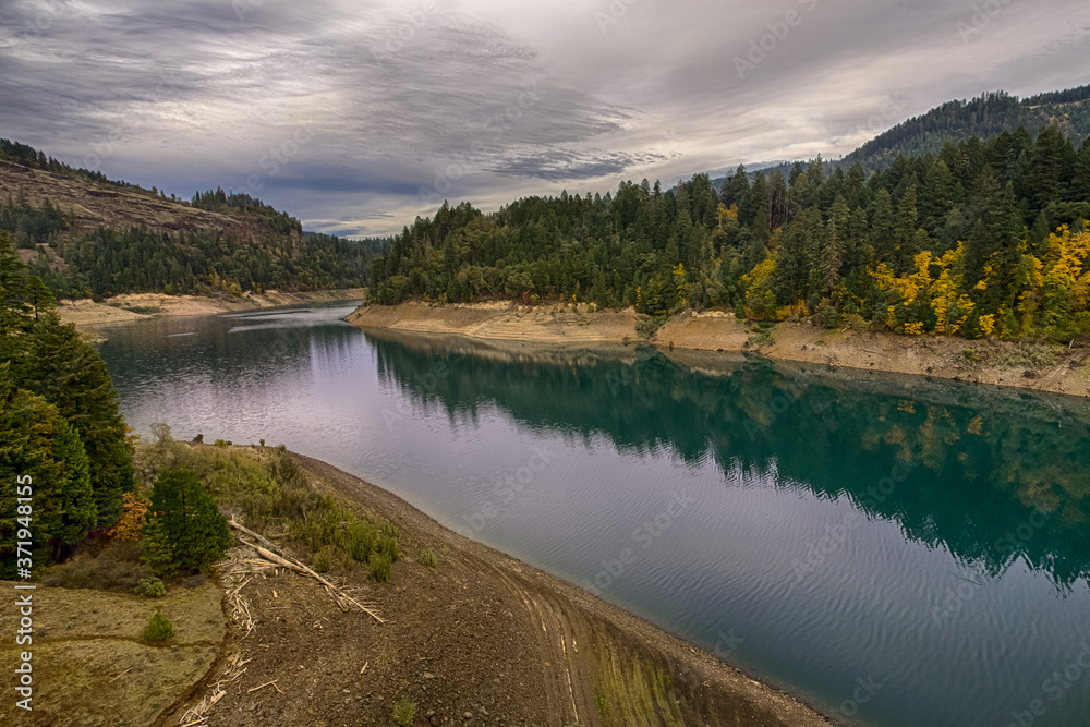 Fototapeta premium Beautiful autumn river landscape in South Oregon, USA. Moody sky and vivid colors foliage reflect in calm river water