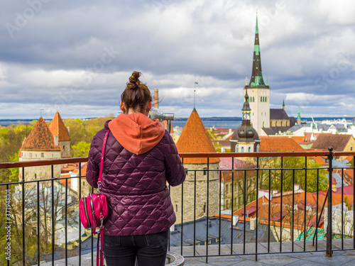Tourist in Estonia, taking photo of old town with smartphone. Travel photography with mobile phone. travel and photography concept, young beautiful woman in red looks towards city towers. copy space
