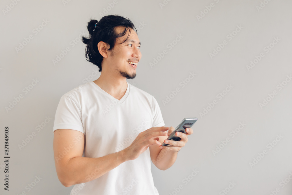 Happy long hair Asian man in white casual t-shirt is using smartphone. Happy long hair Asian man in white casual t-shirt is using smartphone.