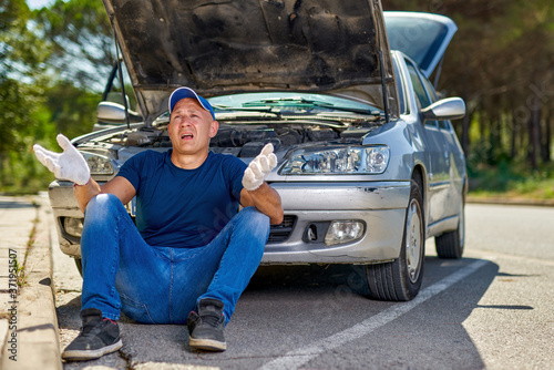 Upset driver man in front of old automobile broken car in city road.