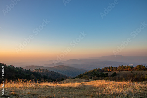 A separate bench in between the hills of Nagy-Szénás mountain in Hungary, misty view on the forests, just before sunset