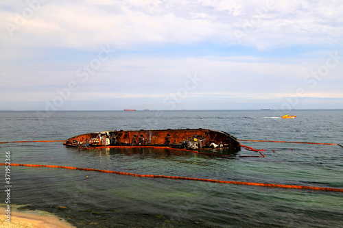 An old rusty tanker flooded and lies in Odessa, Ukraine. Oil spills from the ship and pollutes the sea water. Environmental pollution, water resources, environmental disaster.