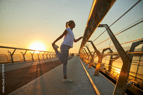 Charming woman stretching legs on the bridge during sunrise
