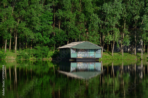 Wooden house on the river with reflection in it, surrounding by trees