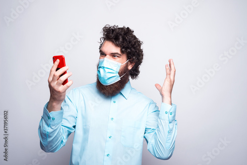 Photo of young man looking amazed at smartphone while wearing medicinal mask.