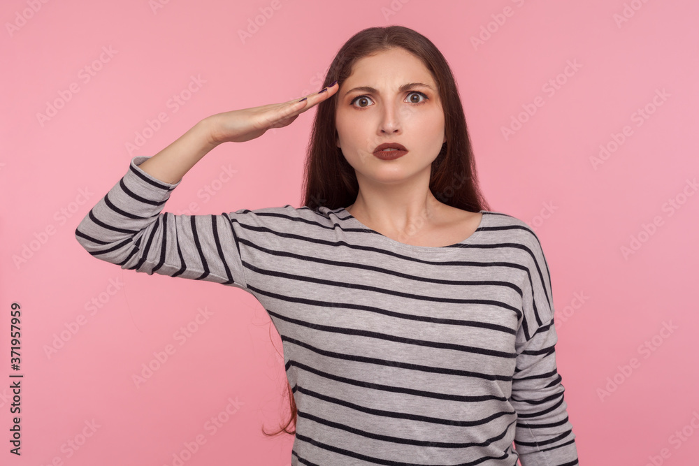 Yes sir! Portrait of responsible patriotic woman in striped sweatshirt following discipline, saluting to commander with hand near temple and listening order. studio shot isolated on pink background Yes sir! Portrait of responsible patriotic woman in striped sweatshirt following discipline, saluting to commander with hand near temple and listening order. studio shot isolated on pink background