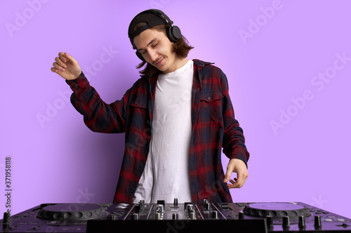 positive male DJ playing music on purple background, caucasian long haired man in casual wear perform club music, wearing headphones