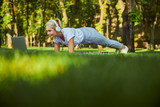 Charming woman doing plank and using laptop in park