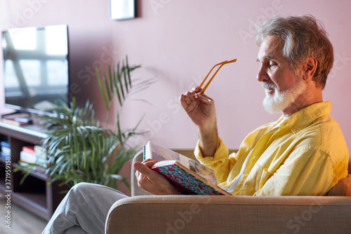 senior caucasian sad man with photo album missing his wife, depressed widower at home