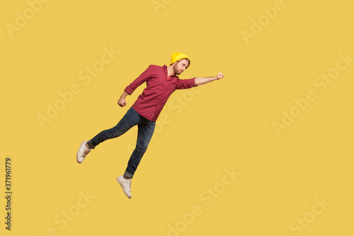 Determined serious ambitious guy flying in air with raised hand, striving forward to victories, feeling super hero power, freedom and confidence to achieve goal. indoor studio shot, yellow background