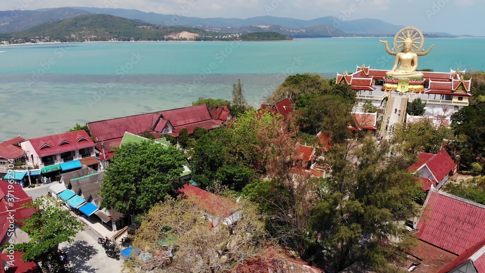 Island with Buddhist temple and many houses. Aerial view of island with Buddhist temple with statue Big Buddha surrounded by traditional houses on stilts in bay of Pacific ocean on Samui, Thailand.