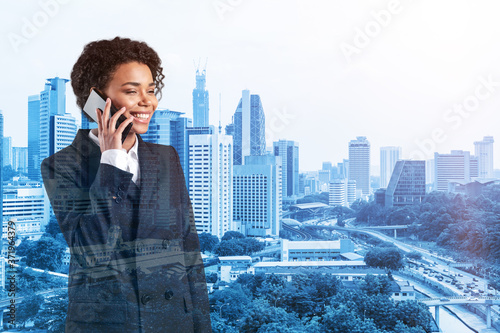 Successful smiling black African American business woman in suit pensively talking phone, Kuala Lumpur cityscape. The concept of consultants as problem solvers. KL skyscrapers. Double exposure. photo