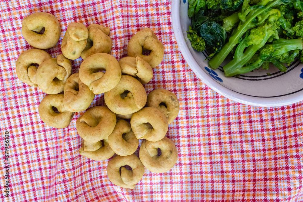 Homemade rapini flavour taralli crackers with bowl full of boiled rapini. Traditional snack food of Puglia