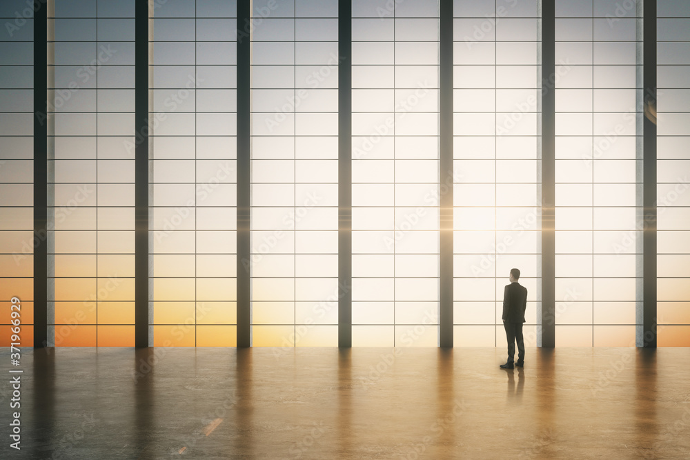 Businessman standing in modern boarding room with sunrise view.