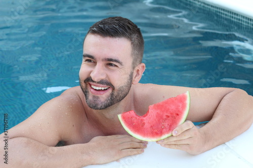Handsome man eating watermelon in the pool 