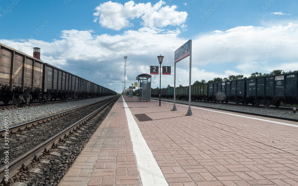 View of the railway tracks from the station platform. Cars standing on the tracks. Freight car. Railway station with a platform. Traveling by rail. View of the railway tracks from the station platform. Cars standing on the tracks. Freight car. Railway station with a platform. Traveling by rail.