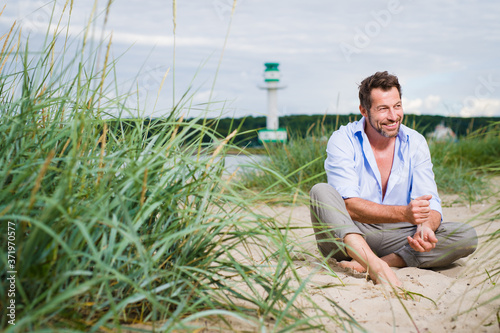 lässiger selbstbewusster Mann sitzt entspannt am Strand im Sand  photo