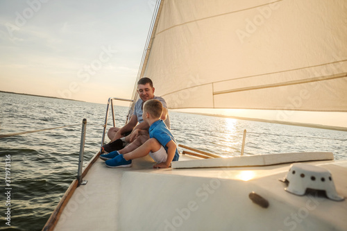 Happy traveler father and son enjoying sunset from deck of sailing boat moving in sea at evening time. Bonding Travel, Summer, Holidays, Journey, Trip, Lifestyle, Yachting concept. 