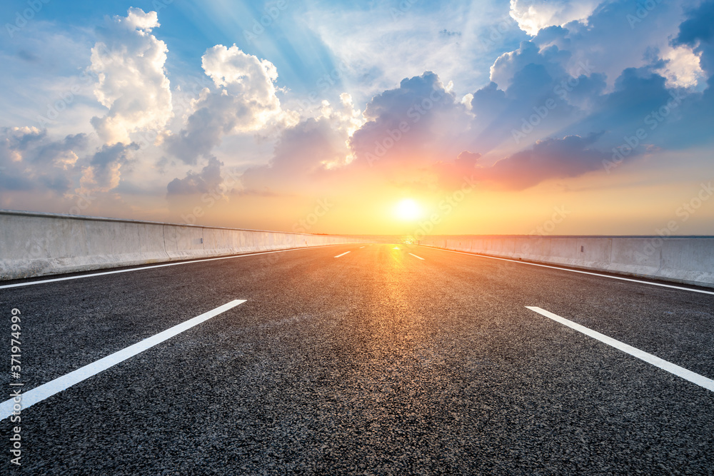 Fototapeta premium Asphalt road and lake with beautiful clouds at sunset.