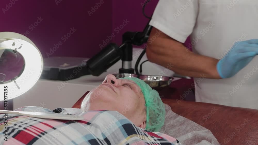 Male doctor removes papillomas of an elderly woman with an electric scalpel. Male doctor removes papillomas of an elderly woman with an electric scalpel.