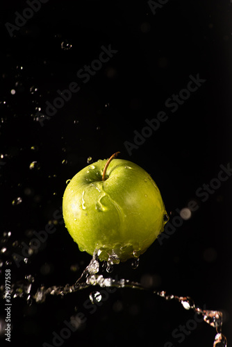 Green apple with beautiful splash of water with black background and selective focus.