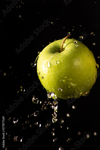 Green apple with beautiful splash of water with black background and selective focus.