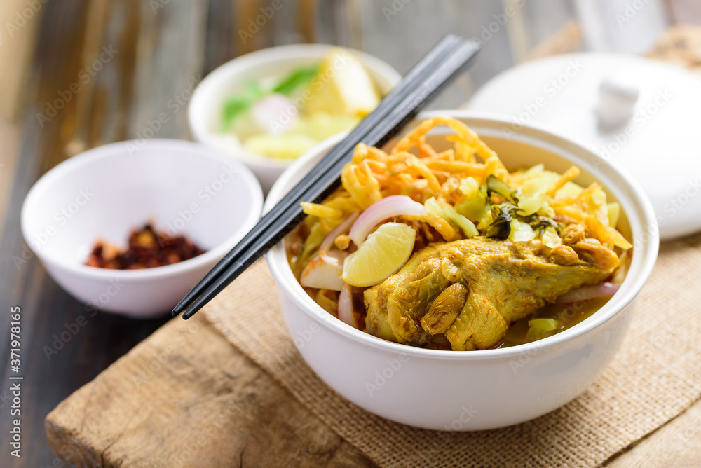 Northern Thai food (Khao Soi), Spicy curry noodles soup with chicken in a bowl eating with crispy deep-fried egg noodles, pickled mustard, shallots, lime and ground chillies fried in oil Northern Thai food (Khao Soi), Spicy curry noodles soup with chicken in a bowl eating with crispy deep-fried egg noodles, pickled mustard, shallots, lime and ground chillies fried in oil