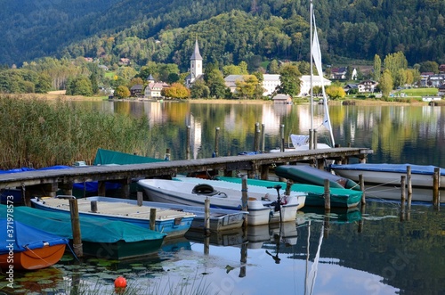 Ossiacher lake in Kaernten (Carinthia), Austria, colorful rowing boats next to a wooden jetty, the village of Ossiach in the background, autumn landscape, a sunny day photo