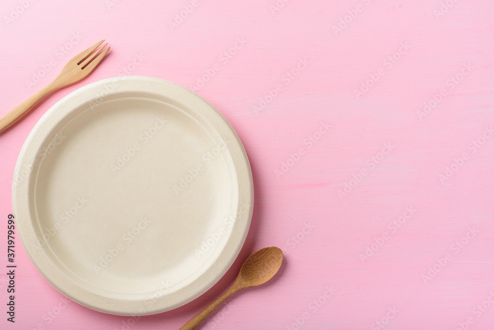 Biodegradable plate, Compostable plate or Eco friendly disposable plate with wooden fork and spoon on pink background Biodegradable plate, Compostable plate or Eco friendly disposable plate with wooden fork and spoon on pink background