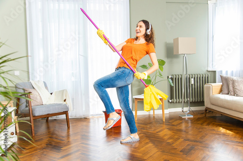 Happy young woman have fun dancing cleaning home