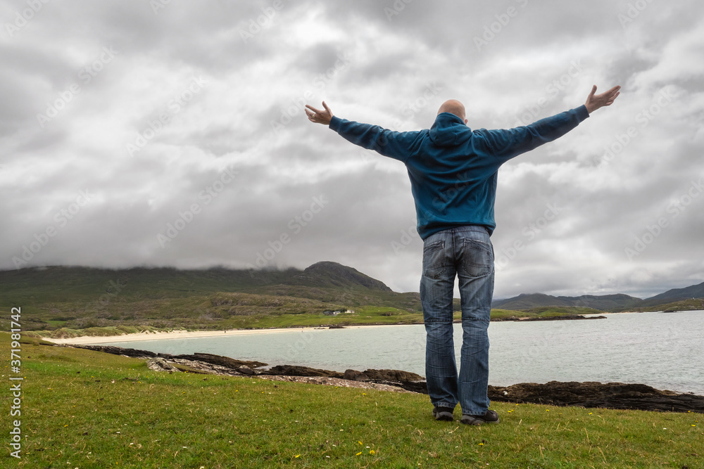 Excited man in blue jacket and jeans with his hand in the air enjoying seascape view. West coast of Ireland. Cloudy sky. Excited man in blue jacket and jeans with his hand in the air enjoying seascape view. West coast of Ireland. Cloudy sky.