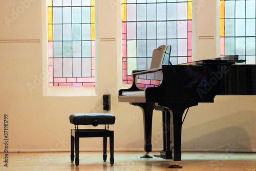 Black piano sits by a stained glass window in a church