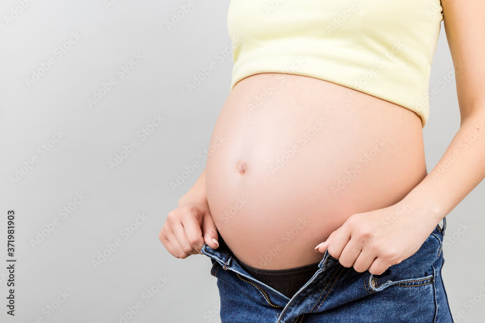Close up of pregnant woman in unzipped jeans showing her naked abdomen at colorful background with copy space Close up of pregnant woman in unzipped jeans showing her naked abdomen at colorful background with copy space