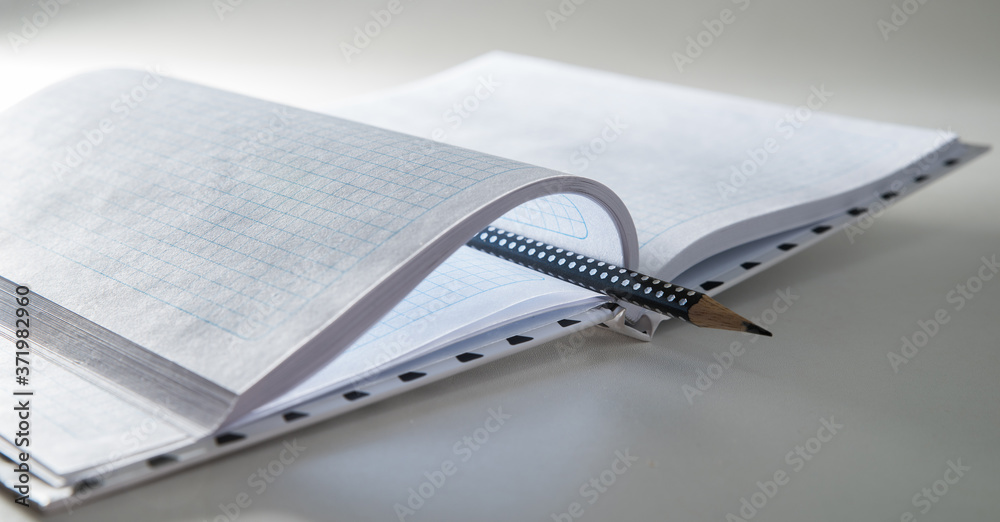 Expanded checkered notebook with open sheets and pencil. Selective focus. Blurred background.