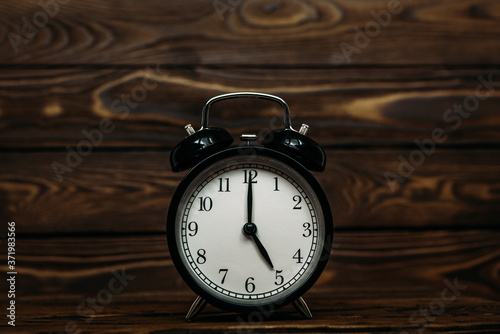 Clock on a wooden background. The clock shows the time of five o'clock in the afternoon. Clock showing the time of five o'clock in the morning. An image of a retro clock showing 05:00 pm/am. 