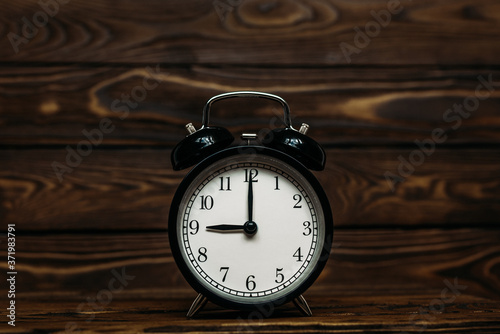 Clock on a wooden background. The clock shows the time of nine o'clock in the afternoon. The clock shows the time of nine o'clock in the morning. An image of a retro clock showing 09:00 pm/am. 