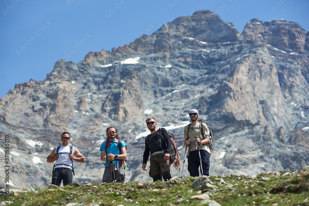 Fototapeta premium From below view of group of four tourists posing with trekking equipment, looking at camera, beautiful mountain Matterhorn with snow on background. Mountain hiking, alpinism. Sport tourism in Alps.