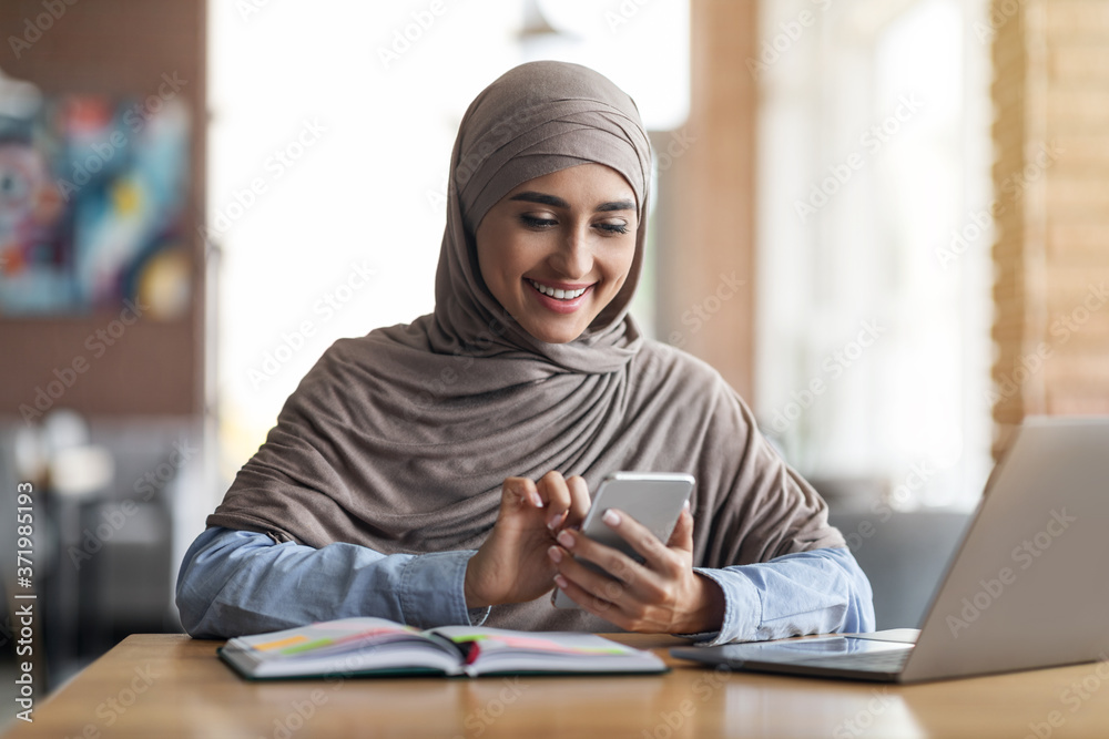 Positive arab woman working at cafe, using phone and laptop Positive arab woman working at cafe, using phone and laptop