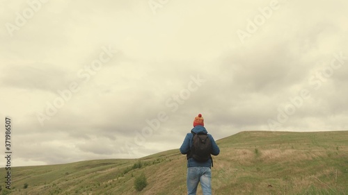A free happy traveler goes to mountains with open arms, catches wind with his hands. young healthy man travels with a backpack enjoying beautiful scenery of mountains and hills. travel concept