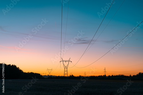 Electricity overhead power lines on a field in a countryside during sunset.