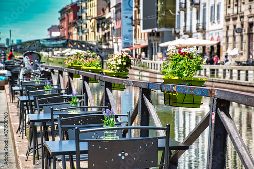 Lovely, romantic restaurant with blooming colorful flowers in pots on the side of Naviglio Grand canal
