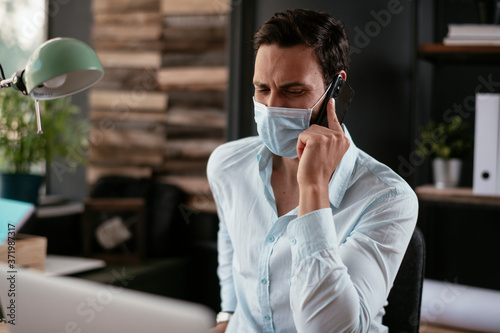 Handsome businessman with medical mask. Young man talking to the phone in office.. © JustLife