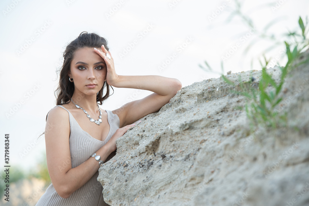 beautiful girl in a light dress stands by the sand dune and looks at the camera