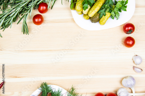 Composition with pickled cucumbers on the white plate, tomatoes, garlic, dill, parsley, rosemary. Cooking food background with free space for text. Top view with copy space