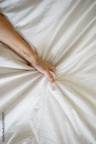 Close up sexy woman hand pulling and squeezing white sheets in ecstasy in bed. Orgasm on white bed. Sex and erotic concept.