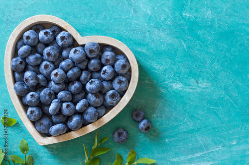 Fresh ripe blueberries in heart shaped bowl on blue background with copy space for your text